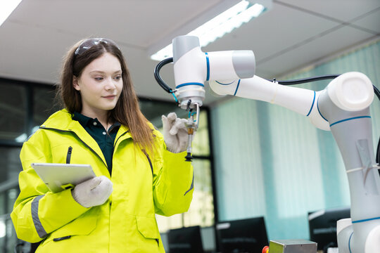 Female engineer operating collaborative robotic arm in smart factory, using tablet for quality control, automation monitoring, highlighting precision engineering, advanced manufacturing technology.