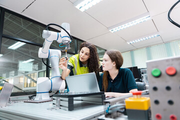 Engaged young woman student engineer in teamwork, learning about robot technology with robotic arm. Future education for industry automation and modern programming for machinery