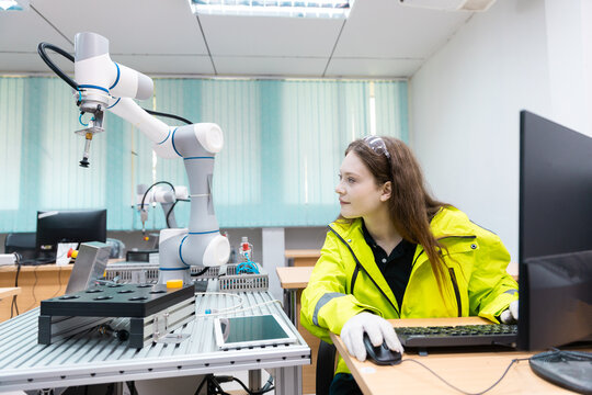 Engaged young woman student engineer in teamwork, learning about robot technology with robotic arm. Future education for industry automation and modern programming for machinery