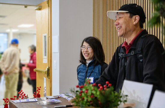 Two volunteers at reception desk. Unrecognizable senior people chatting in the background. California.