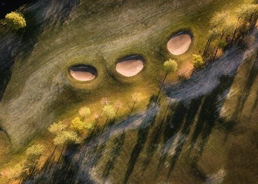 Swords, Ireland - 28 April 2024: Aerial view of Roganstown Hotel Country Club golf course featuring three sand bunkers on green fairways with trees casting long shadows in warm sunlight.