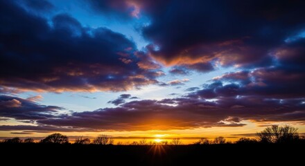 Obraz premium Vibrant sunset with dark clouds and silhouetted trees