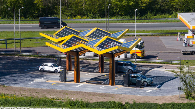 Bant, Netherlands - 21 April 2026: Aerial view of the Fastned charging station with its iconic yellow solar canopy and electric cars parked at the charging points near a highway.