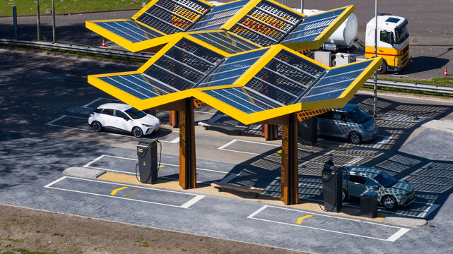 Bant, Netherlands - 21 April 2026: Aerial view of Fastned Charging Station with its distinctive yellow solar canopies and electric vehicles parked at a highway rest area.