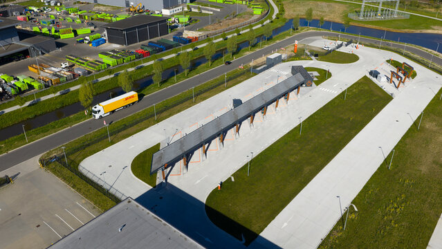 Zwolle, Netherlands - 23 April 2026: Aerial view of Milence Charging Hub Zwolle with its distinctive long roof, surrounding green lawns, and a DHL truck driving on the adjacent road.