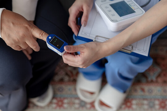 Nurse checking patient oxygen saturation using pulse oximeter attached to finger during medical examination with clipboard and blood pressure monitor feeling calm confident professional healthcare