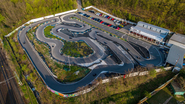 Prague, Czechia - 21 April 2026: Aerial view of the KartPlanet go-kart track featuring winding asphalt lanes, tire barriers, and a parking area surrounded by lush green trees and a railway line.