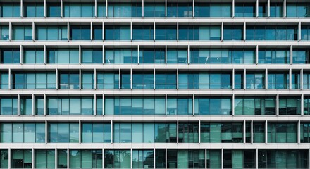Obraz premium A close-up view of a modern building's facade with many windows and glass panels reflecting blue light in the city.