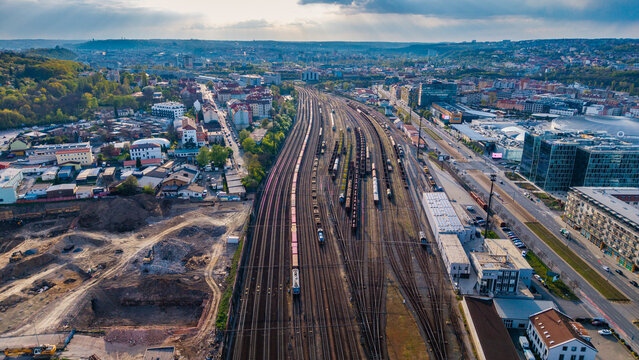 Praha, Czechia - 21 April 2026: Aerial view of a large marshalling yard with freight trains on multiple tracks surrounded by urban buildings and green hills under a cloudy sky.