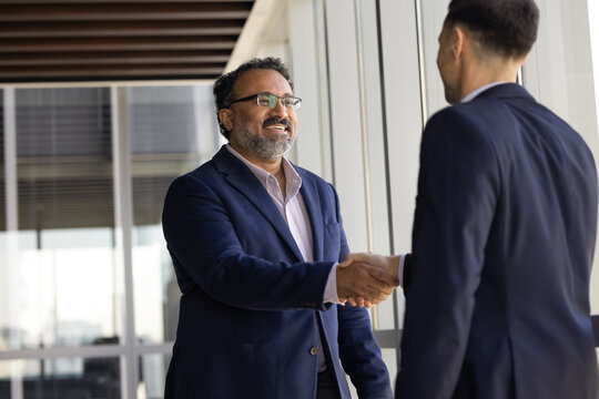 Two smiling businessmen in suits handshaking, as symbol of trust building, closing deal or greeting, starting business meeting in company office. Agreement, successful collaboration and partnership
