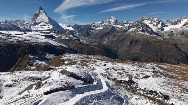 Aerial flyover alongside the Gornergrat railway in Zermatt, Switzerland with a view of the Matterhorn and a train riding down on a snowy autumn day in the Swiss Alps