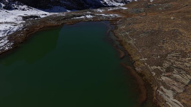 Aerial flyover over Riffelsee lake at Gornergrat in Zermatt, Switzerland with a pan up view towards reflection of the famous Matterhorn on the water surface on a snowy autumn day