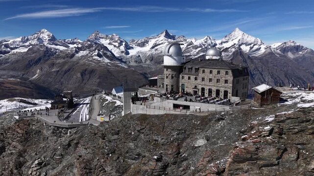 Aerial flyover alongside the observatory of Gornergrat in Zermatt, Switzerland with a view of the Matterhorn and Gorner Glacier on a snowy autumn day in the Swiss Alps