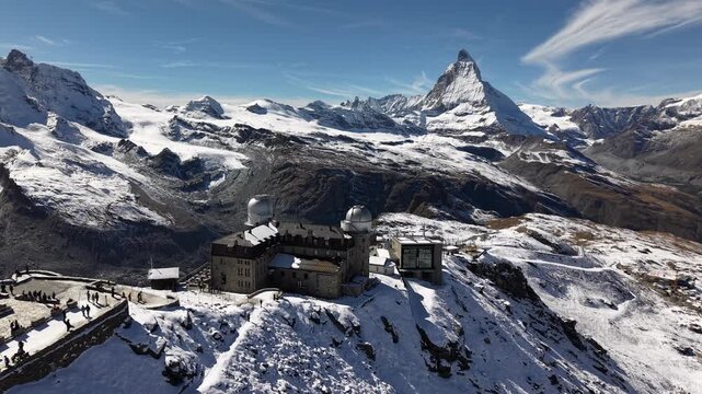 Aerial flyover over the observatory of Gornergrat in Zermatt, Switzerland with a view of the Matterhorn and a train riding down the railway on a snowy autumn day in the Swiss Alps
