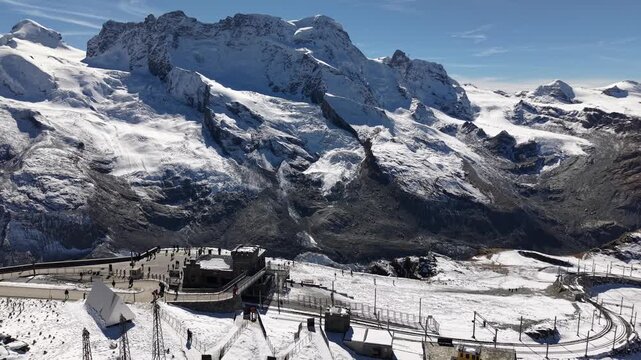 Aerial flyover next to the observatory of Gornergrat in Zermatt, Switzerland with a view of the train station and Dufourspitze mountain peaks a snowy autumn day in the Swiss Alps