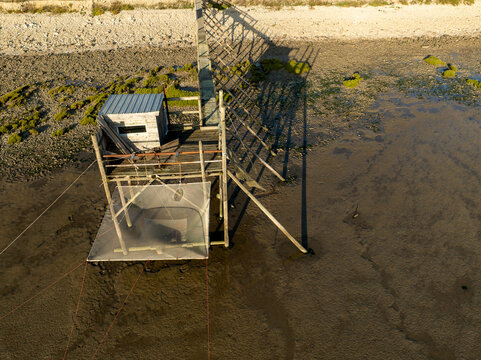 Yves, France - 22 September 2023: Aerial view of a traditional fishing hut on stilts with a large square net on the muddy shoreline at low tide.