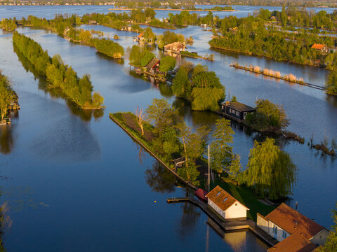 Breukelen, Netherlands - 25 April 2026: Aerial view of Scheendijk islands with small cottages and lush green trees surrounded by calm water during sunset.
