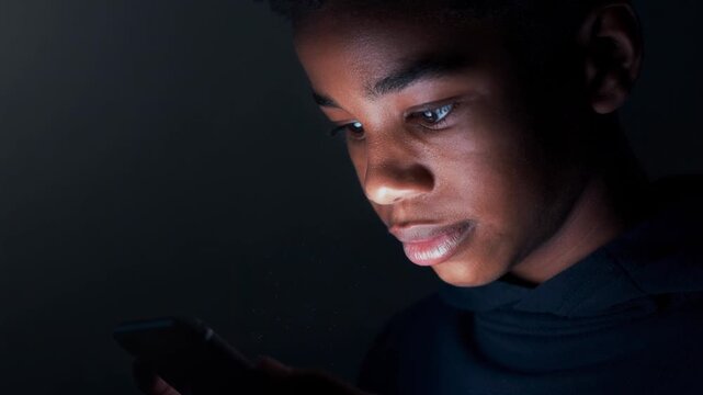 Young person glowing softly from phone screen in dark room fully absorbed in digital content