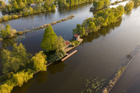 Breukelen, Netherlands - 25 April 2026: Aerial view of Scheendijk recreational area featuring narrow strips of land with small cabins surrounded by calm water and lush green trees at sunset.