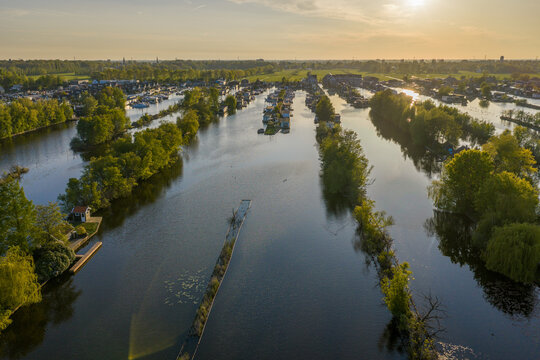 Breukelen, Netherlands - 26 April 2026: Aerial view of Scheendijk houseboats along the narrow waterways surrounded by lush green trees during a golden sunset.