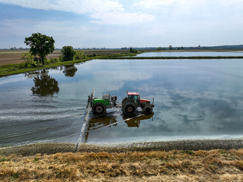 Aerial view of a tractor working in flooded rice fields with sky reflections on the water surface Trino, Piedmont, Italy.