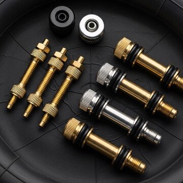 Close-up view of bicycle valve stems and caps for tire inflation, featuring brass and silver components on a dark background, illustrating bike maintenance parts.