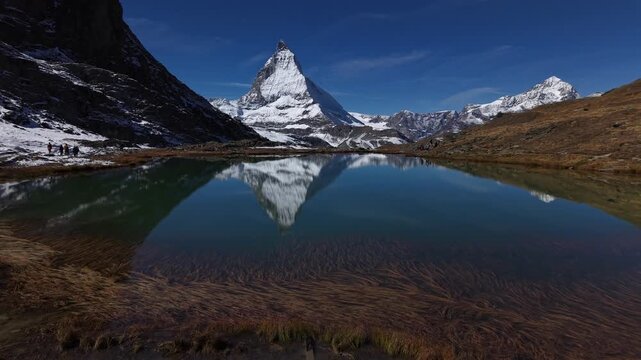 Aerial flyover over Riffelsee lake at Gornergrat in Zermatt, Switzerland with a reflection of the famous Matterhorn on the water surface as a tourist enjoys the view