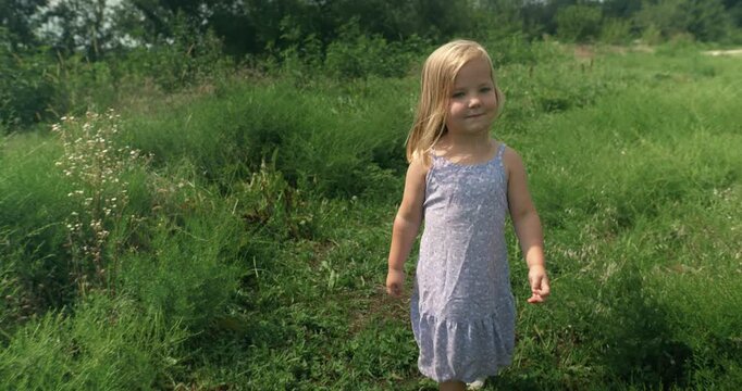 A child walks steadily through a wide green field, immersed in nature. The shot emphasizes openness and calm.