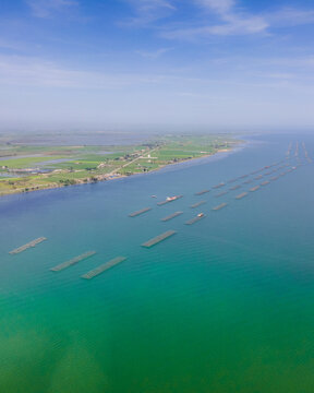 Aerial view of the Ebro Delta showing aquaculture mussel farms in turquoise water along the green coastline of Catalonia, Spain.