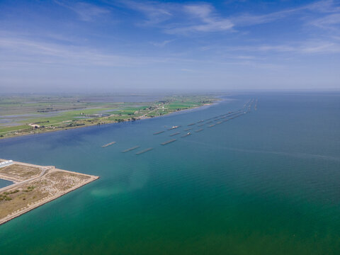 Aerial view of Ebro Delta with mussel farming rafts in the turquoise sea under a blue sky in Catalonia, Spain.