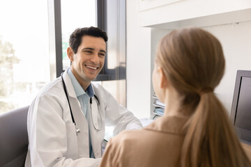 Smiling physician sits at workplace desk lead conversation with woman patient during medical...