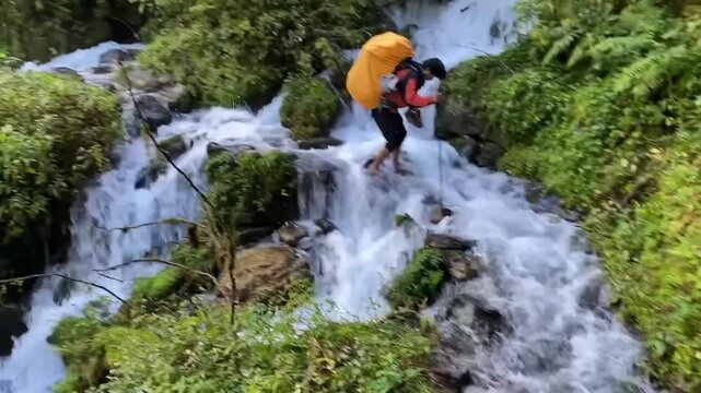Brave Nepali porter crosses raging glacier melt cascade near Kangchenjunga Base Camp, Nepal, capturing Himalayan trekking adventure, floodwaters, wilderness survival and remote mountain travel.