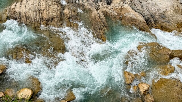 Aerial view of fast river rapids rushing over rugged rocks, whitewater foam and turquoise currents, dramatic natural texture for outdoor adventure and nature themes