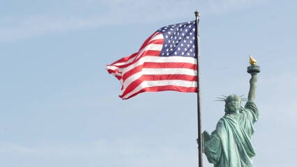 Statue of Liberty on Liberty Island, New York, United States. Cooper monument from behind, democracy and patriotism symbol near Manhattan, NYC USA. American flag waving in wind. Independence concept. © Dogora Sun