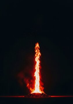 Powerful, brilliant column of orange and red light erupting from a massive outdoor wood pyre against the deep, dark night, pyre, outdoor, element