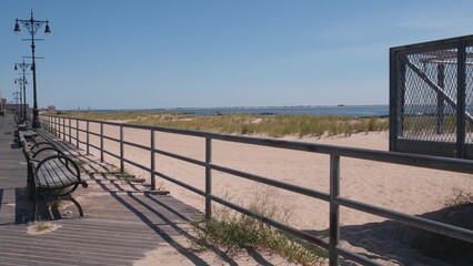 Fototapeta premium Coney Island beach promenade in Brooklyn, New York, United States. Wooden boardwalk near retro luna park. Benches on ocean coast, sandy beach. Waterfront summer holiday in NYC, USA. Outdoor recreation