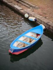 Obraz premium Small blue rowboat moored at a stone canal quay wall during a calm summer day