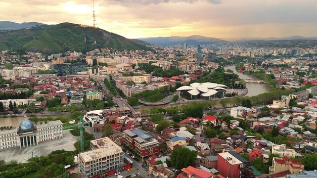 drone Aerial of the Public Service Hall in Tbilisi, Georgia. Modern architecture along the Mtkvari River with the historic city skyline and Caucasus mountains at sunset