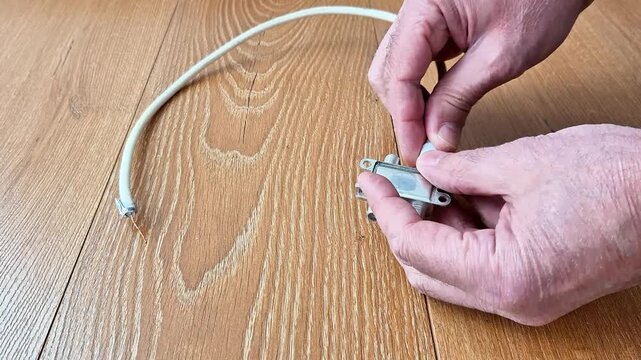 Hands connecting a coaxial cable to a metal splitter on a wooden surface, demonstrating installation and setup for distributing television or internet signal connections