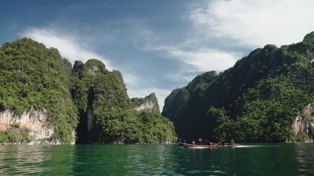 Cinematic Wide Shot of Traditional Longtail Boat Navigating Through Towering Limestone Karsts and Emerald Waters, Scenic Landscape of Khao Sok National Park, 4k Stock Video