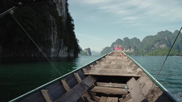 Cinematic POV from Traditional Longtail Boat Prow Sailing Past Massive Limestone Cliffs, Emerald Water and Distant Karst Mountains, Khao Sok National Park, 4k Stock Video