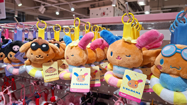 Rows of Sanrio character plush keychains featuring USAHANA and Pompompurin in summer swim ring outfits hanging on a retail display rack on May 9, 2026 in Bangkok, Thailand.