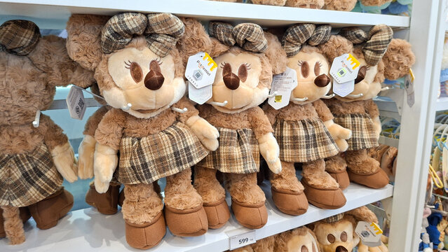 Row of cute Minnie Mouse plush dolls wearing brown plaid dresses and matching bows displayed on retail shelf on May 6, 2026 in Bangkok, Thailand.