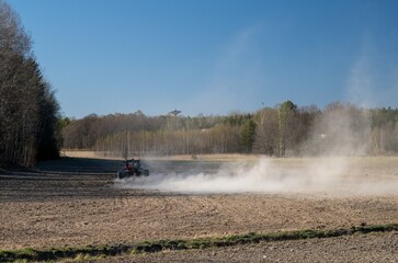 Fototapeta premium tractor plowing dry agricultural field raising dust cloud during spring farming season rural landscape concept