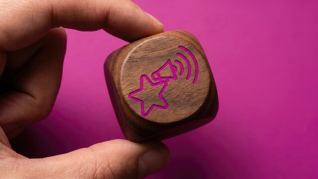 A wooden cube with a star-person megaphone amplify icon held by hand on a vivid fuchsia background, symbolizing influencer marketing and reach amplification.