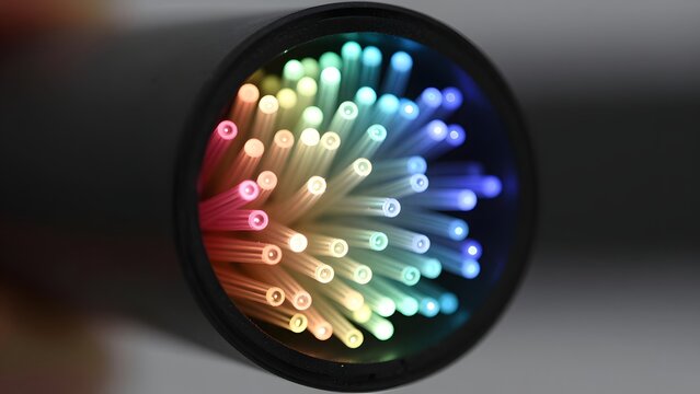 43. A photorealistic macro close-up of fiber optic cables in cross-section showing dozens of individual glass fibers each glowing with transmitted light in varying colors, individual fiber tips showin