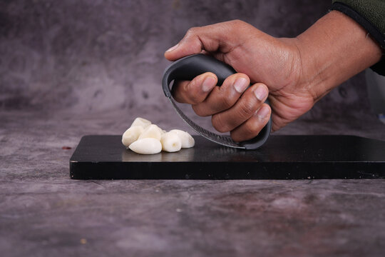 Close-up of a hand using a rocker grater to crush garlic cloves on a black cutting board