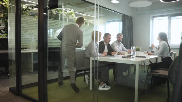 A view through a glass partition shows a modern, busy office interior. Job interview process is in office. Human resources, meeting and group of hiring candidates for vacancy