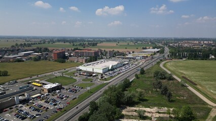 Obraz premium Urban Sprawl: An aerial view showcases a sprawling commercial area adjacent to a highway, featuring a large shopping center and parking lots, surrounded by fields and residential zones.