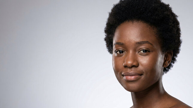 Close-up portrait of a cheerful young Black woman with a natural hairstyle, smiling confidently at the camera against a simple background